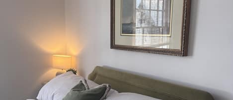 A neatly made bed with white and green pillows, a green blanket, and a framed picture on the wall.