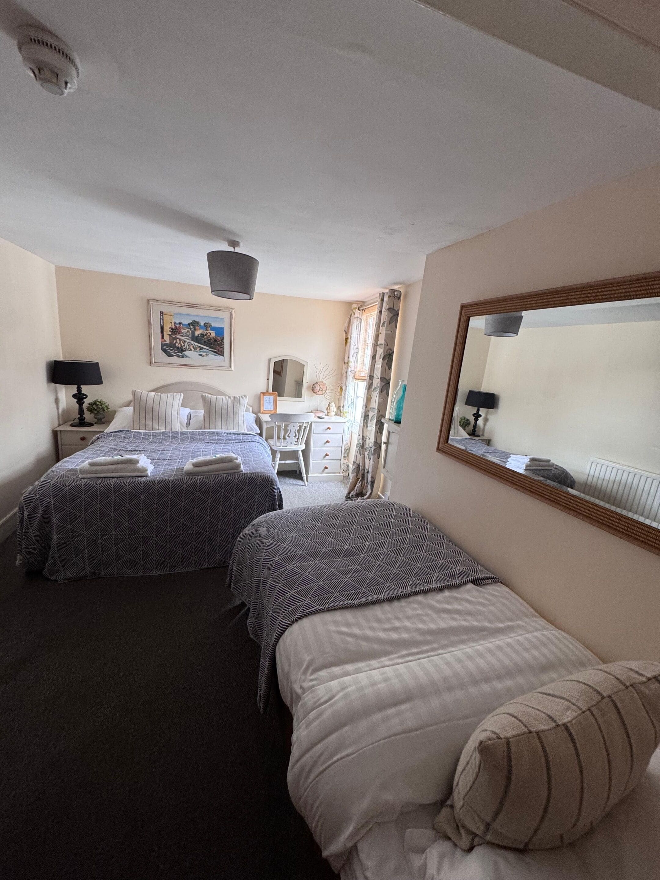A hotel room with two beds, a desk, a chair, a mirror, and a ceiling light fixture.