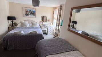 A hotel room with two beds, a desk, a chair, a mirror, and a ceiling light fixture.