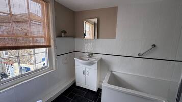 A bathroom with a window, a sink, a mirror, a shower, and a towel.