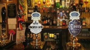 A bar with multiple taps labeled 'Cask Marque,' 'Proper Job,' and 'Tribute.' - The Ship Inn (Mevagissey)