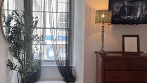 A room with a window, a potted plant, a wooden dresser, a television, and a patterned rug. - The Ship Inn (Mevagissey)