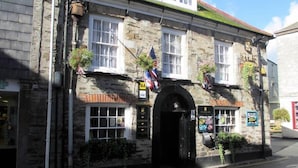 A stone building with a black entrance, windows, and a sign indicating a quiz event. - The Ship Inn (Mevagissey)