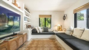 Ein Wohnzimmer mit einem großen Flachbildfernseher, einer Couch, einer Fensterbank und einem Bücherregal.