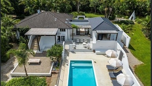 Ein modernes Haus mit Schwimmbad, Sitzgelegenheiten im Freien und üppiger Bepflanzung.