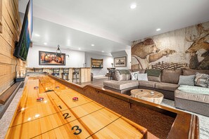 Une pièce comprenant une table de jeu de palet, un coin bar, un canapé et une fresque murale.