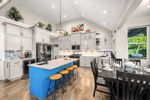 Une cuisine moderne avec des meubles blancs, un îlot de couleur bleue et un coin repas comprenant une table et des chaises.