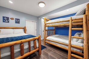 Habitación con literas de madera y una cama individual, ambas con ropa de cama blanca. Hay dos adornos en la pared, uno con un ancla y otro con una pala, y la palabra 'LAKE'.