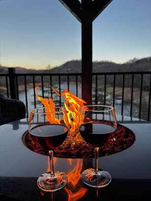 Dos copas de vino tinto sobre una mesa, con un fuego de fondo.