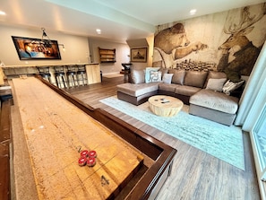 Ein Wohnzimmer mit einer Shuffleboard-Bahn, einem Sofa, einem Couchtisch und einem Wandgemälde.