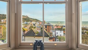 A room with a large window overlooking a coastal town, featuring a view of the sea and buildings.