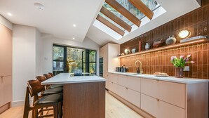 A modern kitchen with a large island, wooden chairs, and a view of the outdoors through large windows.