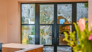 A modern kitchen with a large island, a dining area with chairs, and a stone wall with a view of the garden.