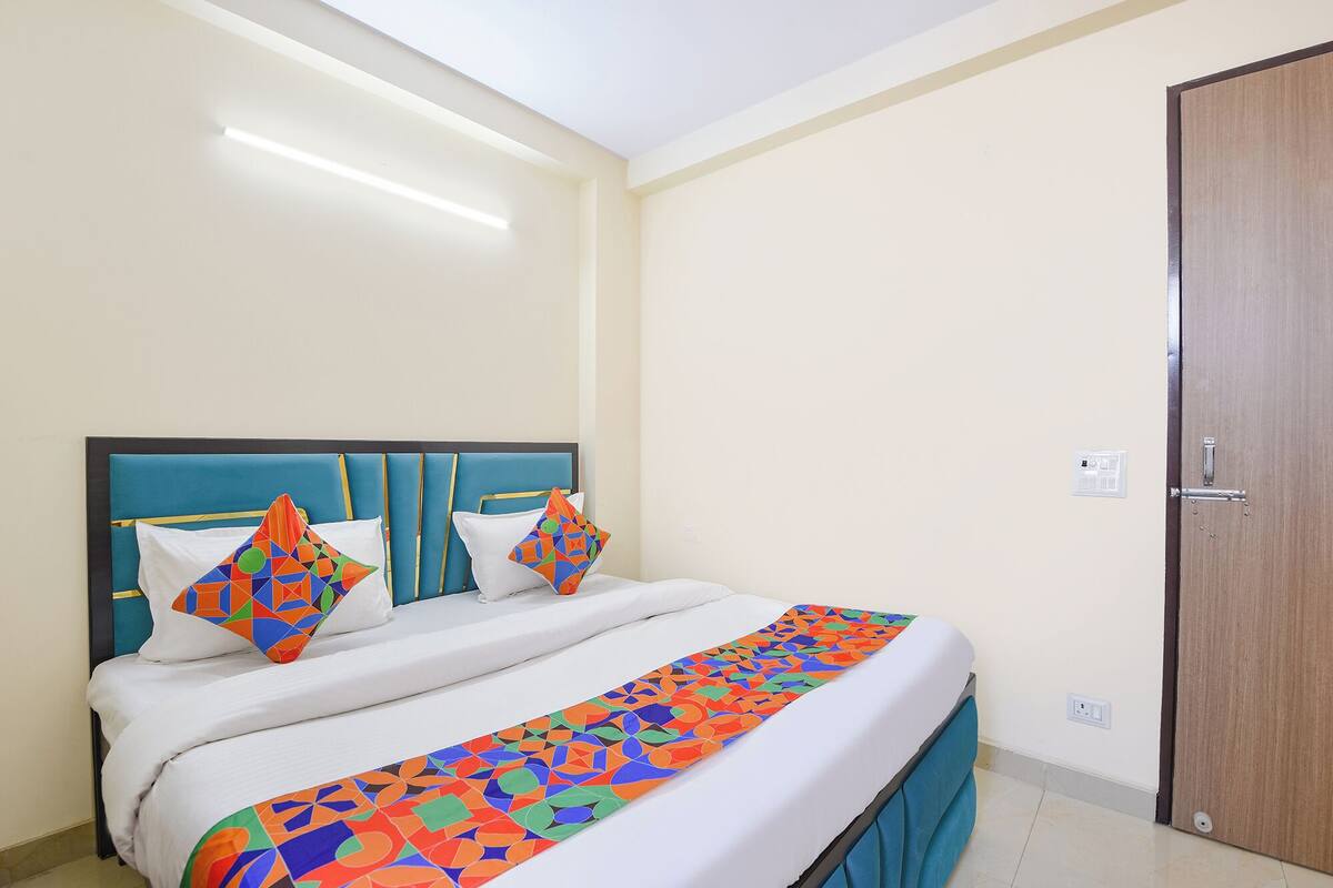 A neatly made bed with a colorful geometric-patterned bed runner, a headboard with a teal accent, and a wooden door to the right.