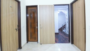 A hallway with three wooden doors, each marked with a number. The hallway has a tiled floor and leads to a staircase with a marble-like wall. - Fabhotel Glass Castle (New Delhi)