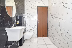 A bathroom with a white sink, a mirror, a wooden door, and marble-patterned walls. - Fabhotel Golden Sapphire (Jaipur)