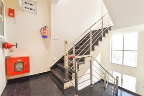 A staircase with metal railings, a fire alarm, and a fire extinguisher on the wall. - Fabhotel Golden Sapphire (Jaipur)