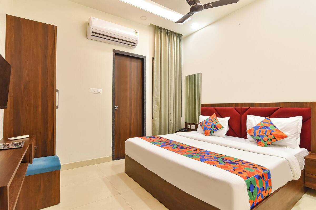 Une chambre d’hôtel équipée d’un lit, d’un bureau, d’un climatiseur, d’un ventilateur de plafond et d’une fenêtre avec des rideaux.