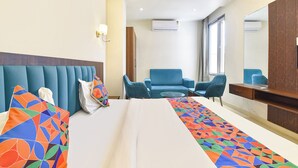 Quarto de hotel com cama, duas cadeiras, escrivaninha e um espelho grande.