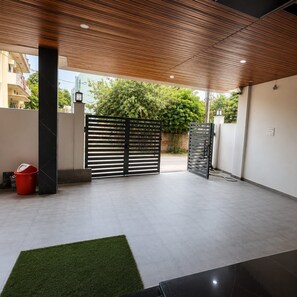 A covered outdoor area with a modern gate, a red bucket, and a grassy patch. - FabHotel The Sarnath Residency (Varanasi)