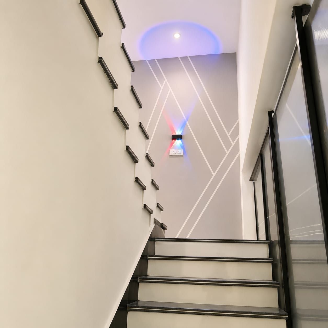 A modern staircase with a geometric wall design and a ceiling light fixture.