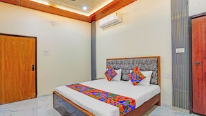 A bedroom with a bed, an air conditioner, a ceiling fan, and a wooden door. - Via The Sarnath Residency (Varanasi)