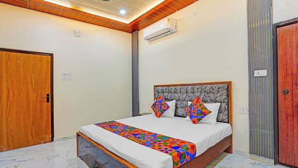 A bedroom with a bed, an air conditioner, a ceiling fan, and a wooden door. - Via The Sarnath Residency (Varanasi)