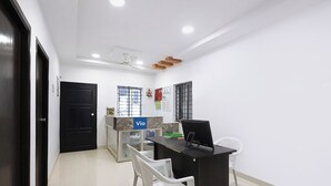 Une pièce comprenant un bureau, deux chaises, un ordinateur noir, une fenêtre avec des barreaux et une porte.