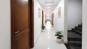 A hallway with wooden doors, potted plants, and a staircase. - FabHotel Expressway 135 - Near By KJR Hospital (Noida)