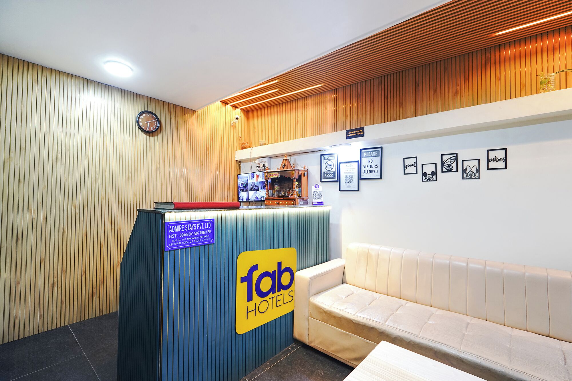 Un área de recepción con una pared de madera, un mostrador de recepción con el rótulo 'Tab Hotels', un reloj y una zona de estar con un sofá.