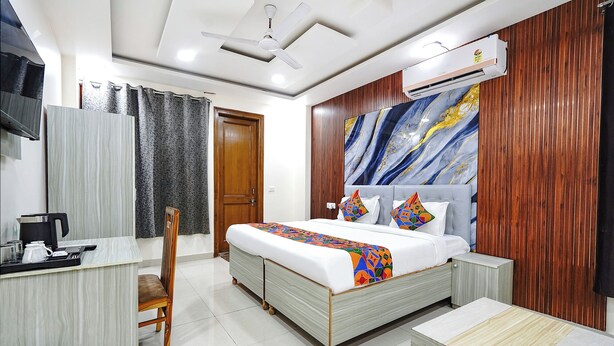 A hotel room with a bed, bedside table, chair, and a desk with a kettle and phone. - FabHotel Expressway 135 - Near By KJR Hospital (Noida)