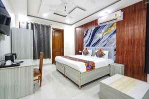A hotel room with a bed, bedside table, chair, and a desk with a kettle and phone. - FabHotel Expressway 135 - Near By KJR Hospital (Noida)