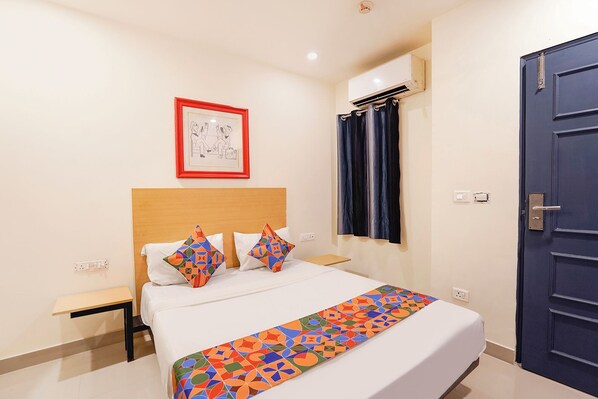 A hotel room with a bed, a nightstand, a framed picture on the wall, a window with curtains, and a door. - Fabhotel Mvr (Ghaziabad)