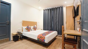 A hotel room with a bed, a desk, a chair, a TV, and a wardrobe. - Fabhotel Mvr (Ghaziabad)