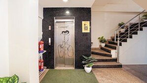 A hotel entrance with a marble wall, a fire extinguisher, a sign prohibiting outside food, and a staircase with potted plants. - Fabhotel Mvr (Ghaziabad)