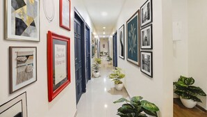 A hallway with framed artwork, potted plants, and blue doors. - Fabhotel Mvr (Ghaziabad)