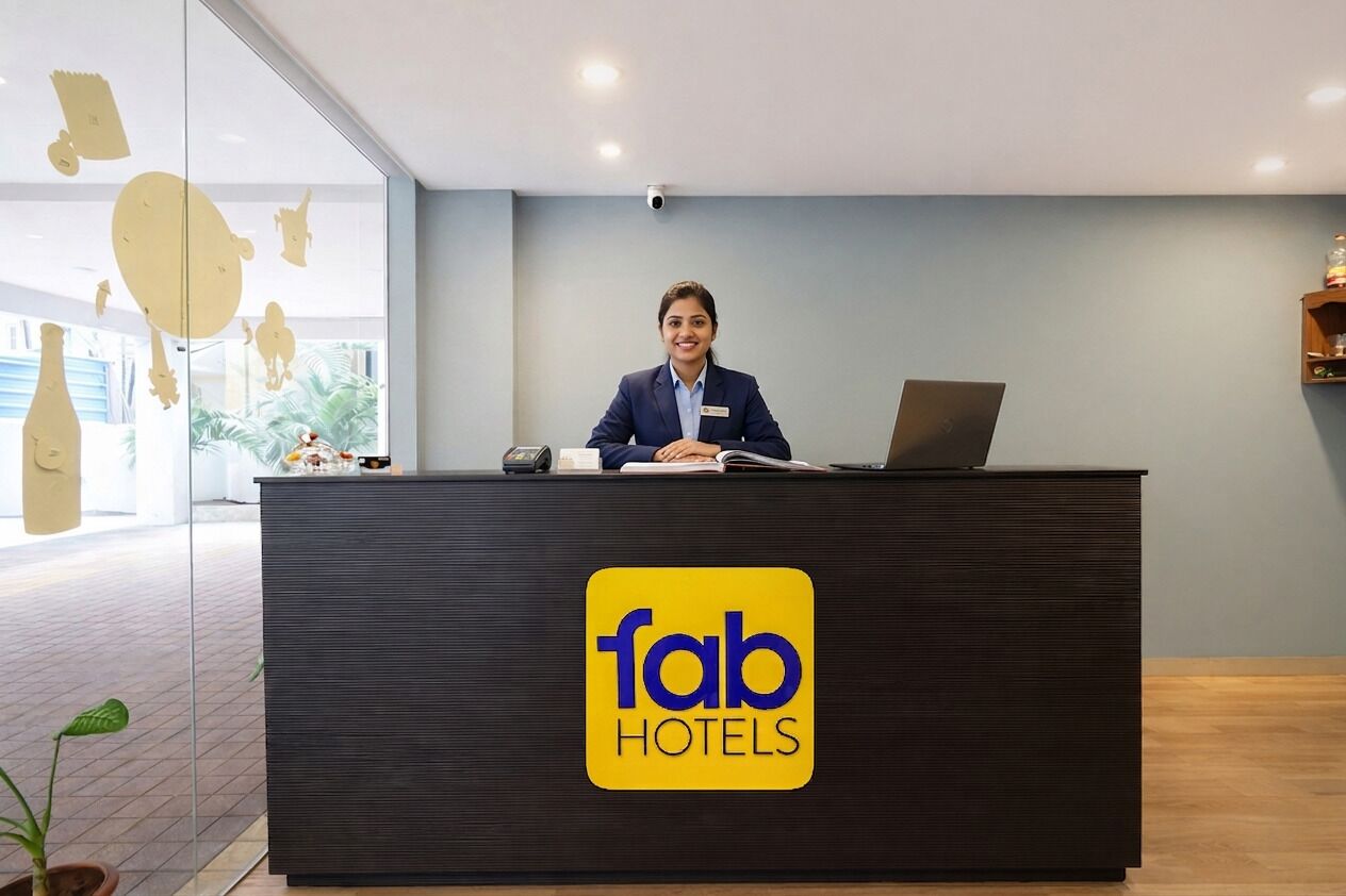 Una recepción con el logotipo de Fab Hotels, una placa identificativa, una computadora portátil y un objeto decorativo pequeño.