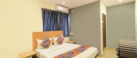 A hotel room with a bed, a bedside table, a chair, a ceiling fan, and a window with curtains.