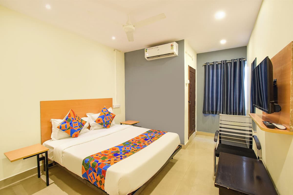 Habitación de hotel con cama, escritorio, silla, televisor y aire acondicionado.