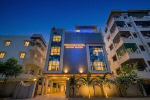 Un hotel de varios pisos con un cartel que dice 'Vedhansi Hotel Luxury Rooms' y 'Tab Hotels'.