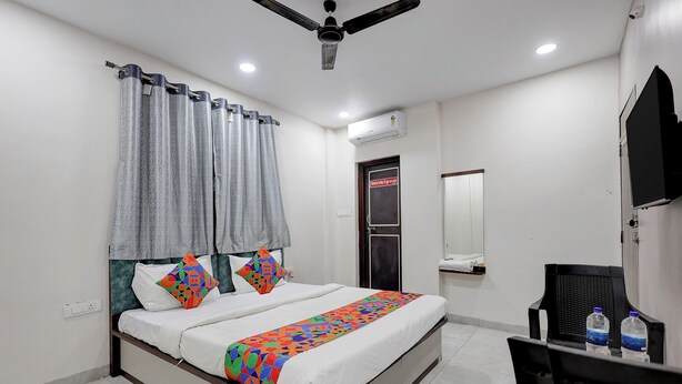 A bedroom with a bed, curtains, a ceiling fan, an air conditioning unit, a mirror, and a desk with a chair. - Fabhotel Welcome Inn Besa (Nagpur)