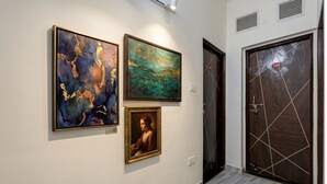 A hallway with three artworks on the wall, a door with a number, and a tiled floor. - Fabhotel Welcome Inn Besa (Nagpur)