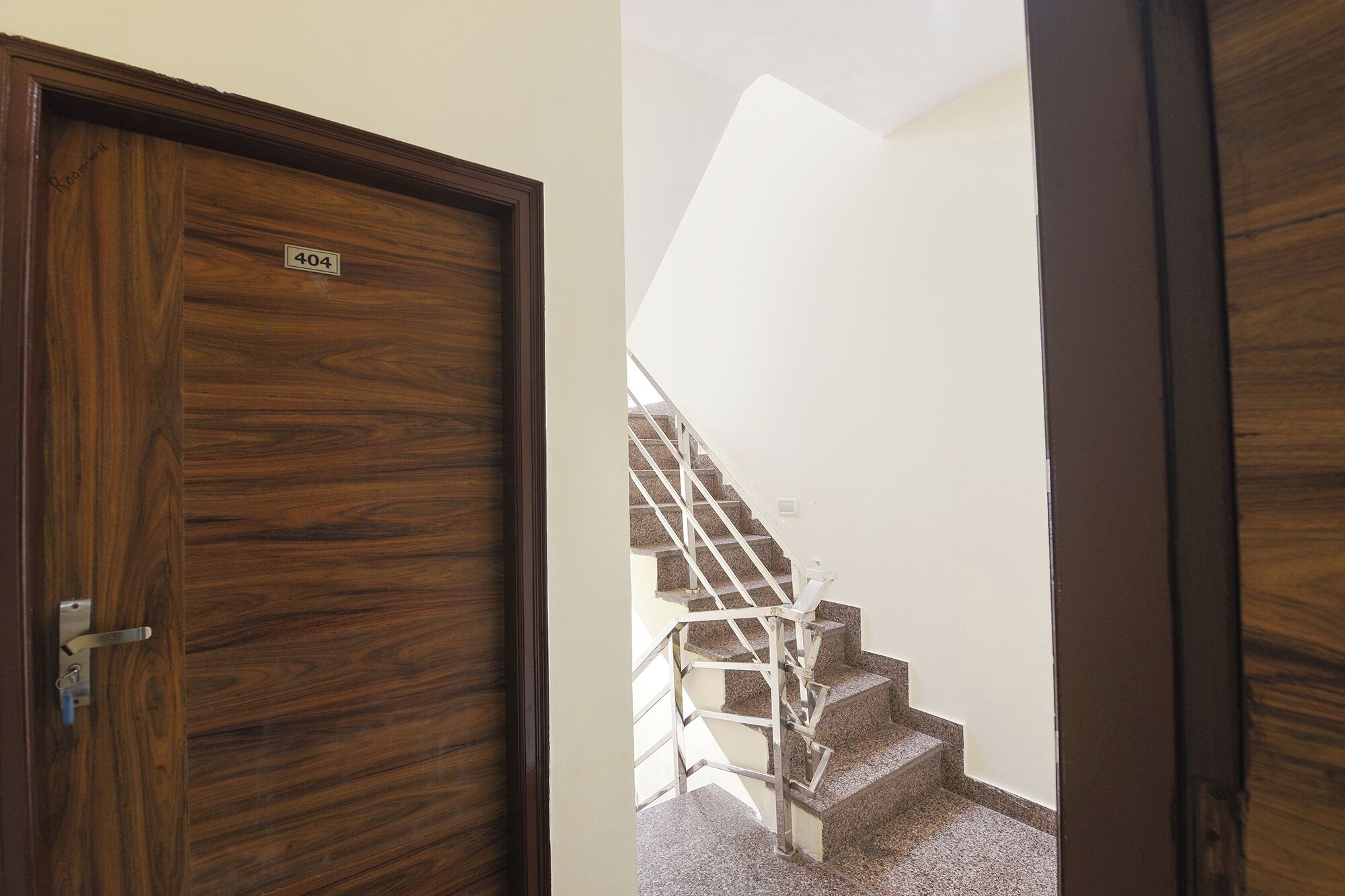 A wooden door with a number plate, a staircase with a metal railing, and a white wall.