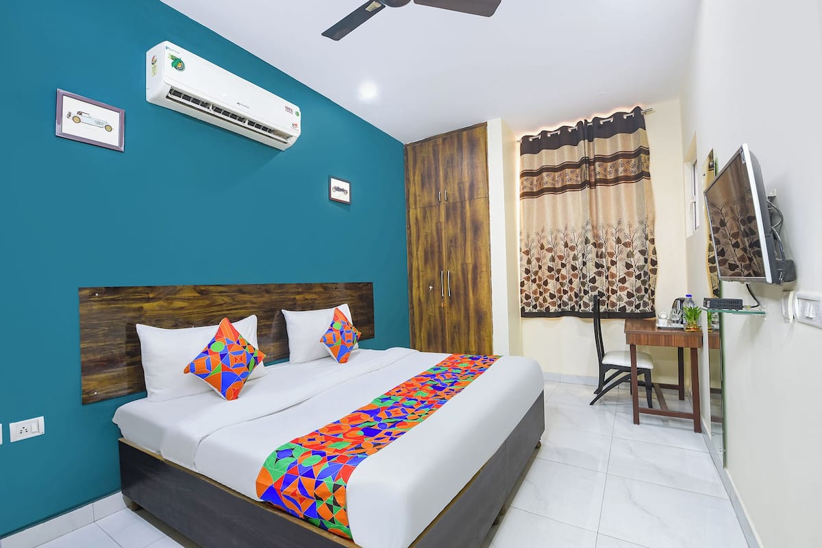 A bedroom with a bed, a desk, a chair, an air conditioner, and a television.