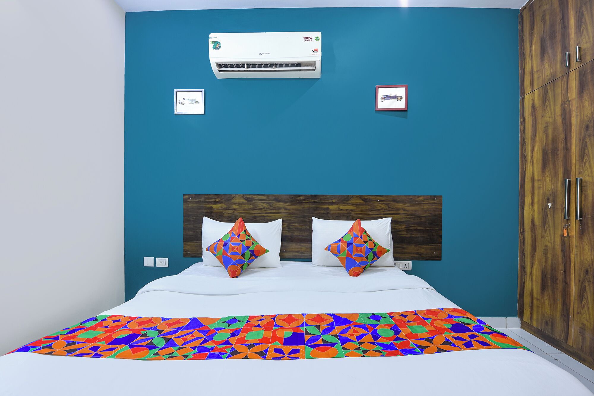 Camera da letto con un letto, due cuscini, una coperta colorata, un condizionatore d'aria e un armadio in legno.