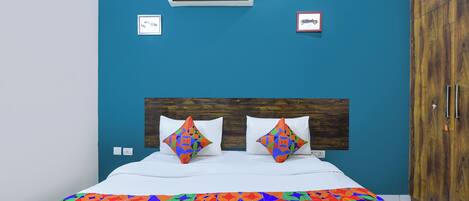 Camera da letto con un letto, due cuscini, una coperta colorata, un condizionatore d'aria e un armadio in legno.