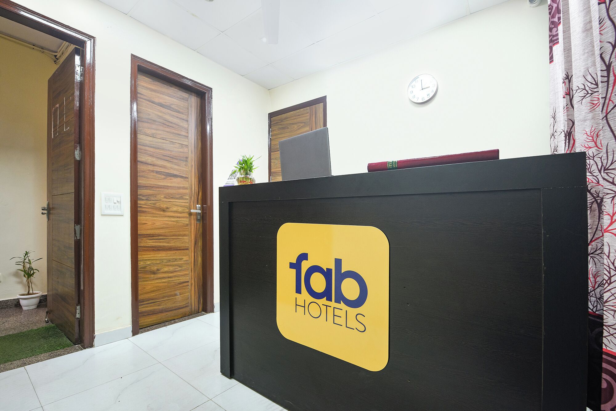 A reception desk with a logo for Fab Hotels, wooden doors, a clock, and a small plant.