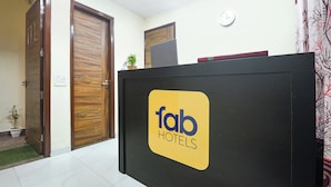 A reception desk with a logo for Fab Hotels, wooden doors, a clock, and a small plant. - FabHotel Royal (Gurugram)