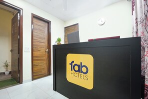 A reception desk with a logo for Fab Hotels, wooden doors, a clock, and a small plant. - FabHotel Arpit Residency (Gurugram)