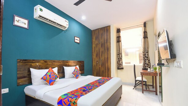 A bedroom with a bed, a desk, a chair, an air conditioner, and a window with curtains. - FabHotel Royal (Gurugram)